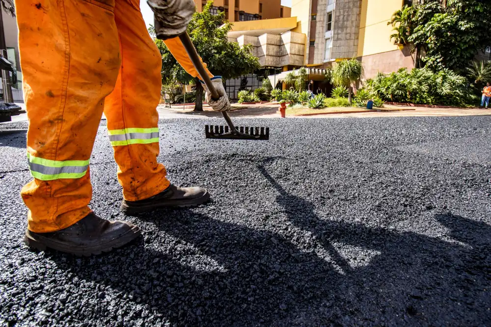 Worker raking hot asphalt during a resurfacing job